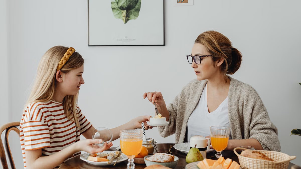A cozy breakfast scene featuring a mother and daughter sharing a meal at a dining table indoors.