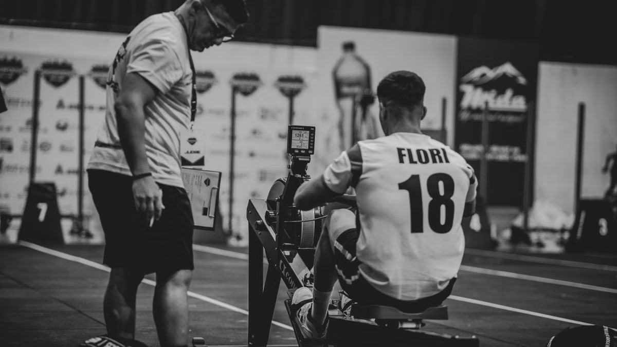 An athlete using a rowing machine indoors, coached in a gym setting.